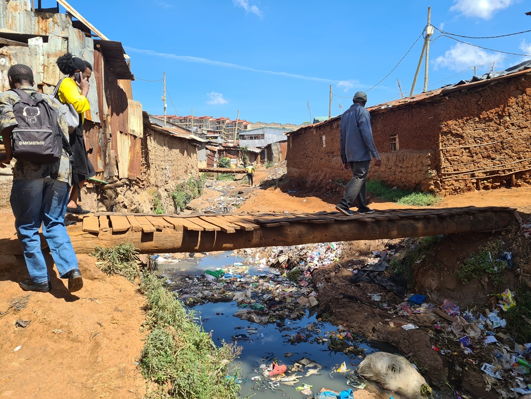 Afrikában a lakosság közel fele nyomornegyedekben él. Ez az arány Mombasában, Kenya második legnagyobb városában még magasabb: az emberek 65%-a lakik ilyen informális telepeken. Ezek a helyek a legalapvetőbb városi infrastruktúrát is nélkülözik: nincs szilárd hulladékkezelés, vezetékes ivóvíz, közvilágítás és burkolt út. Bogo Bogo az egyik legfiatalabb mombasai nyomornegyed, ahol a letelepülők nem tulajdonosai a teleknek, melyen a házuk áll: a terület külföldi magántulajdonban van. A probléma országos méretű, a 2010-es évek óta zajlik a földtulajdonosi viszonyok felmérése az országban, mely során az állam igyekszik visszavásárolni azokat a földeket, amelyen kenyaiak laknak, ezáltal biztosítva tulajdonjogi védelmet nekik. A nyomornegyed házai nagyon változatos képet mutatnak: a téglaépítésűtől kezdve a vályogházon át a hullámpaláig mindenféle építmény megtalálható itt. 